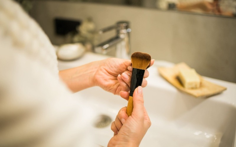 female-hand-holds-makeup-brush-in-bathroom-make-u-2023-11-27-04-57-32-utc-1-scaled-dd058e.jpg